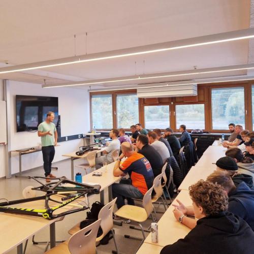 Vortragender spricht zu Gruppe von Zuhörern in einem Schulungsraum mit Fahrradrahmen